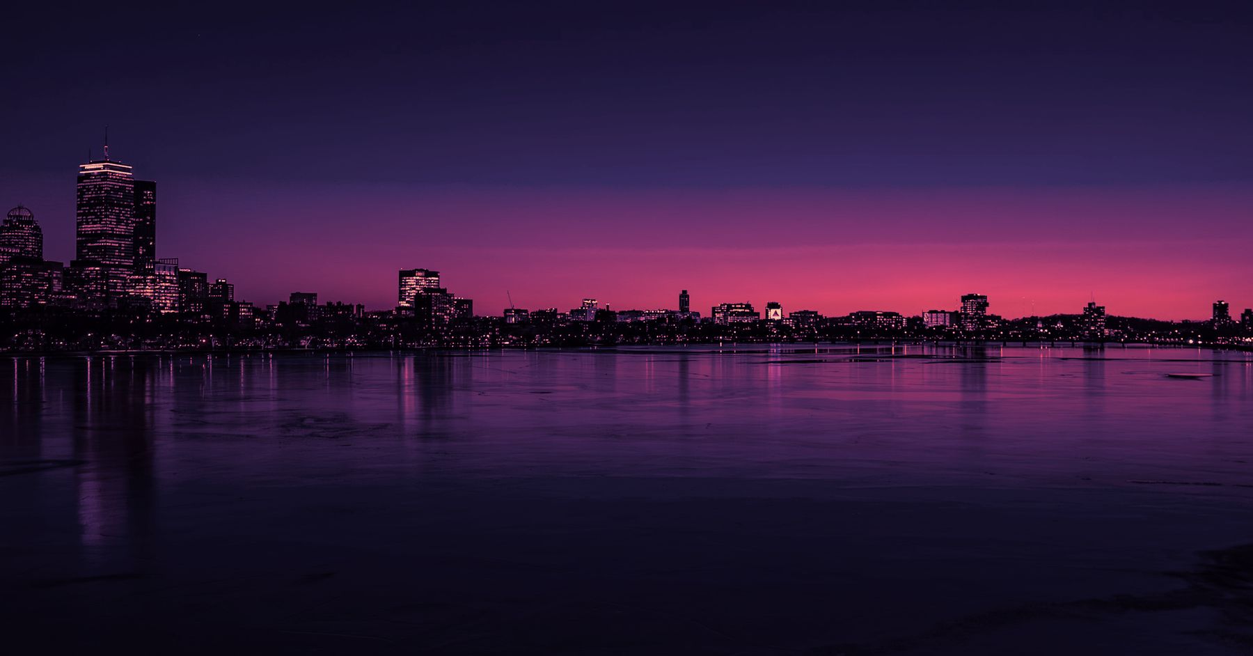 The Boston skyline after sunset, its towers lit across the Charles River